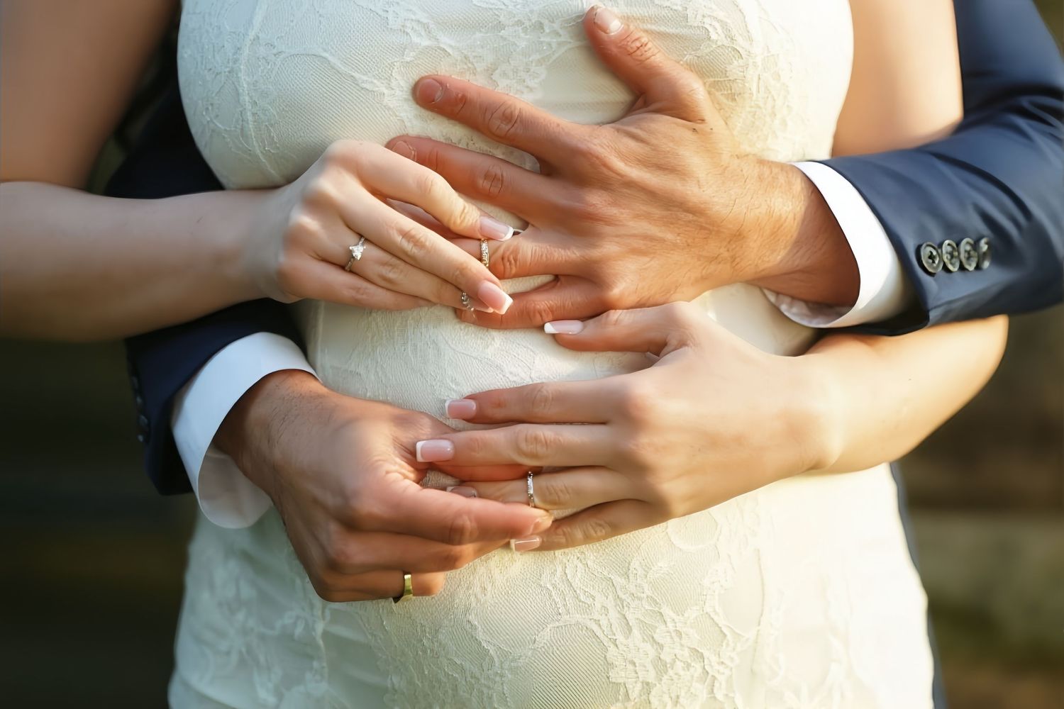Close-up of bride and groom showing wedding rings while embracing in lace wedding dress.
