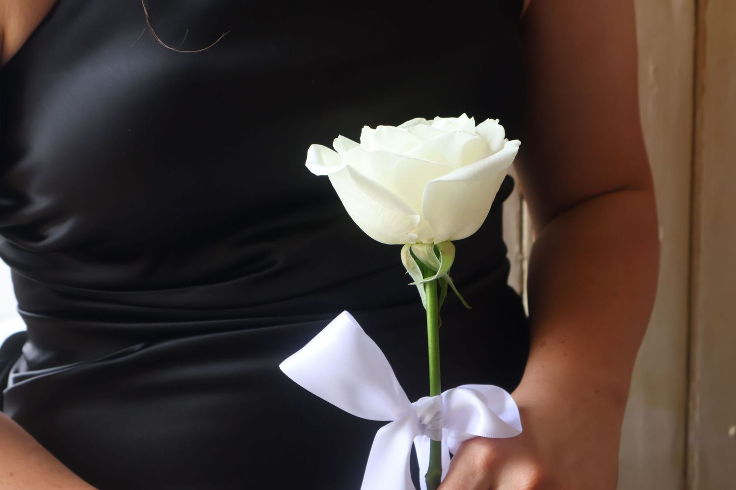 Bridesmaid in black dress holding single white rose with white ribbon bow at wedding.