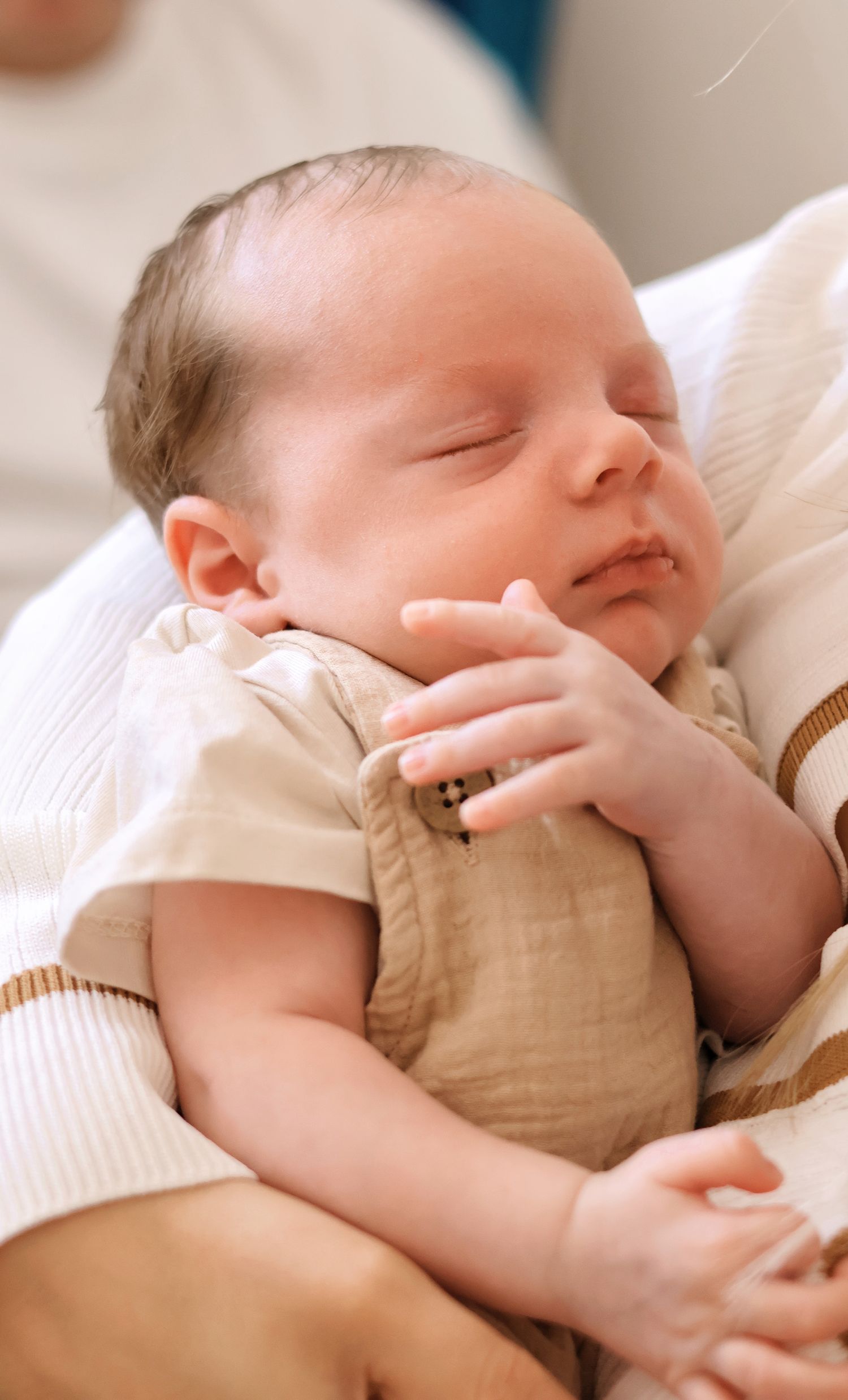 Peaceful sleeping newborn baby in beige romper cradled in parent's arms.