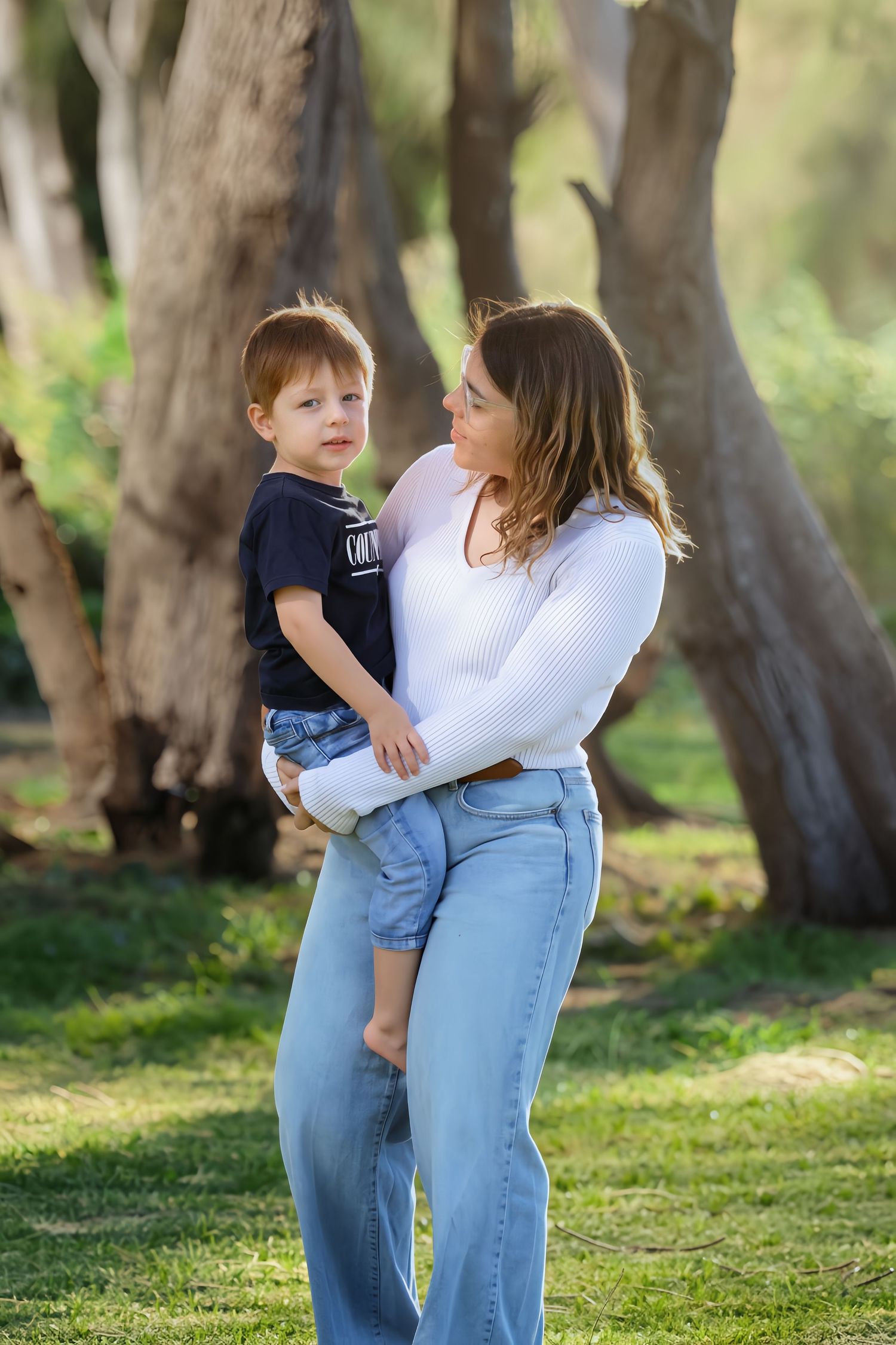 Young mother holding toddler boy in a sunny park, sharing a tender moment outdoors.