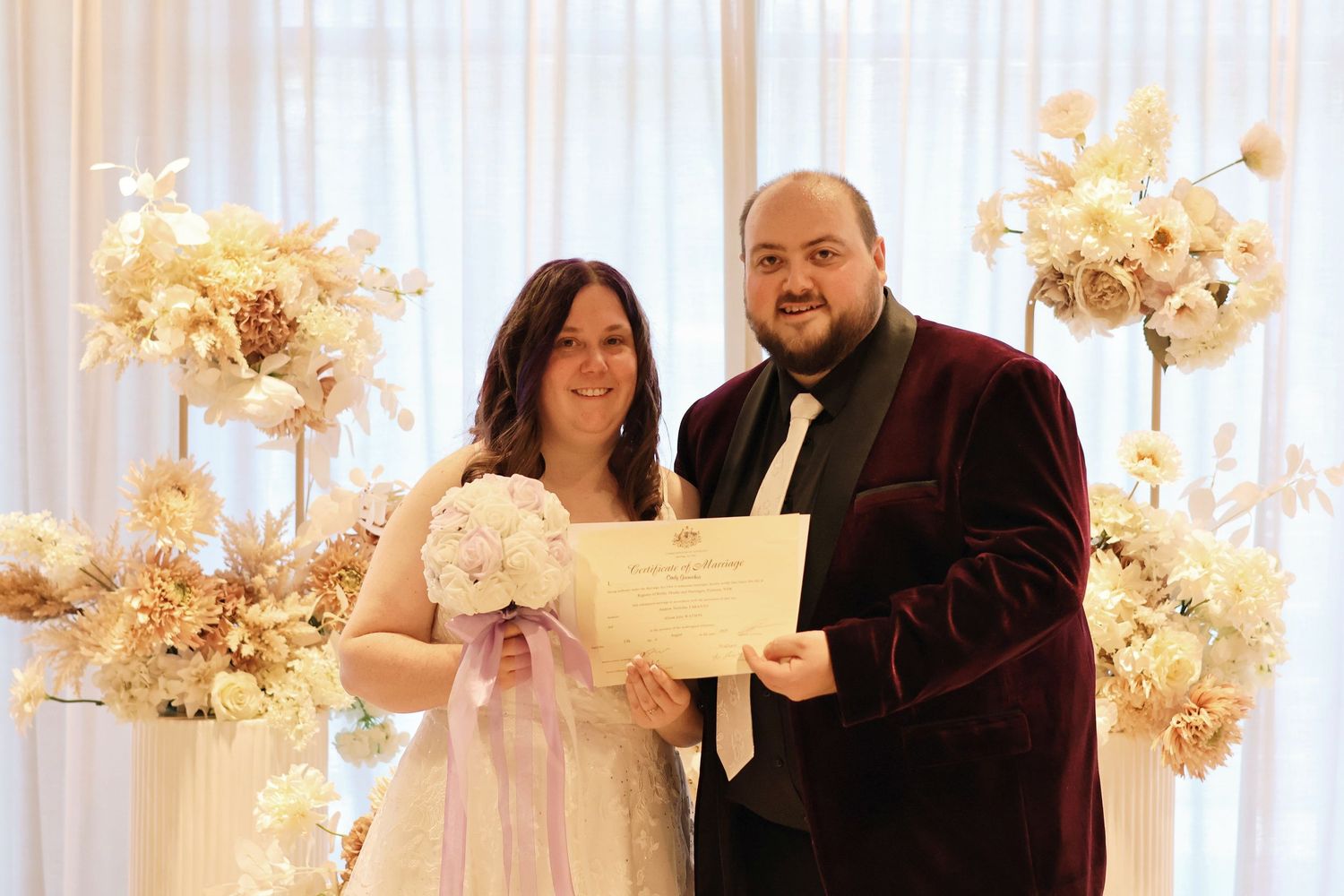 Newlywed couple holding marriage certificate at elegant floral wedding ceremony with white blooms.