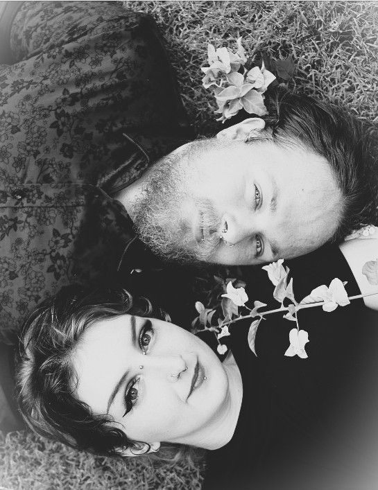 Black and white portrait of couple lying on ground with delicate flowers between them.