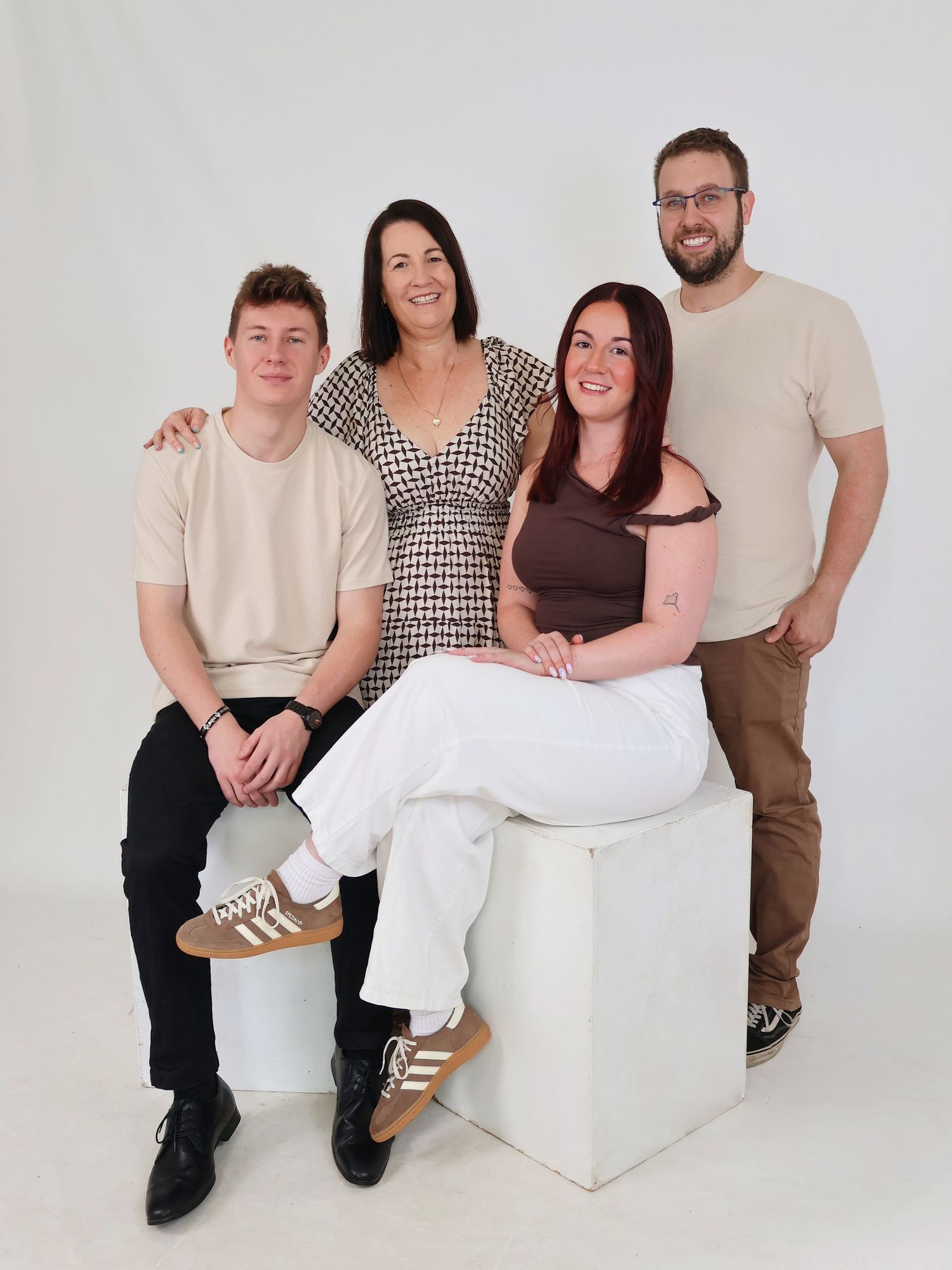 Family of four posing together in a bright studio, two seated and two standing, smiling warmly.