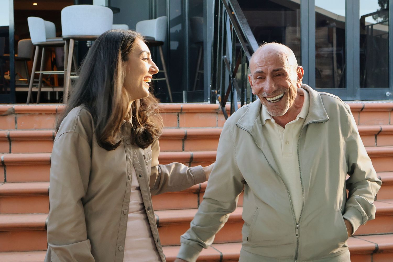 A smiling man and woman laughing together outdoors on brick steps.