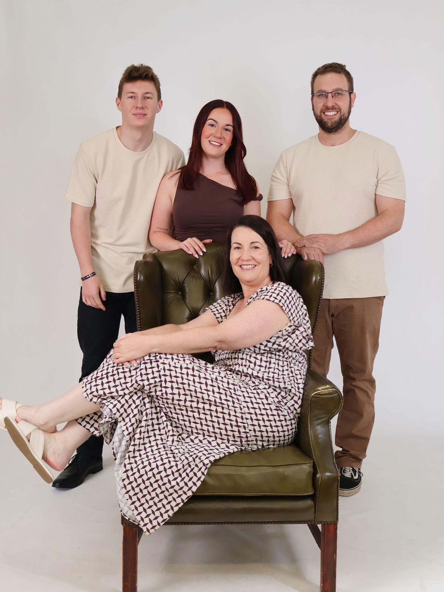 Family of four posing with older woman seated in green leather chair in bright studio setting.