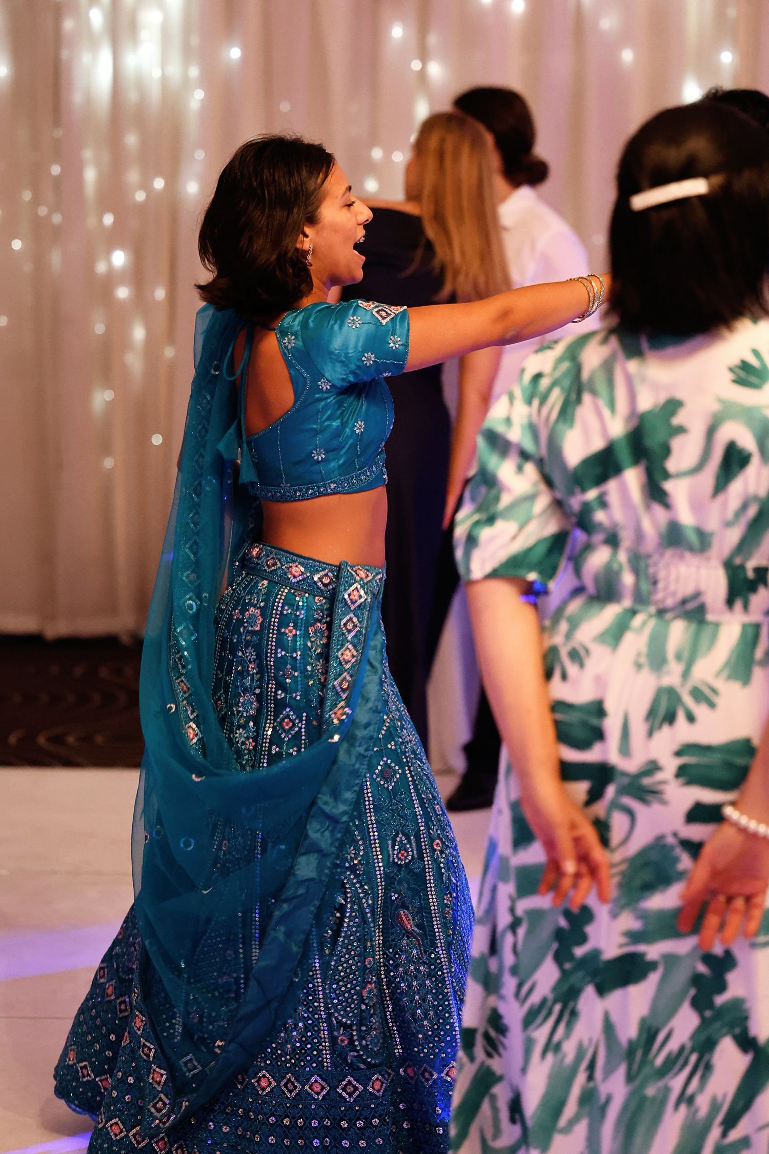 Woman dancing joyfully in a blue embroidered lehenga at a wedding reception.