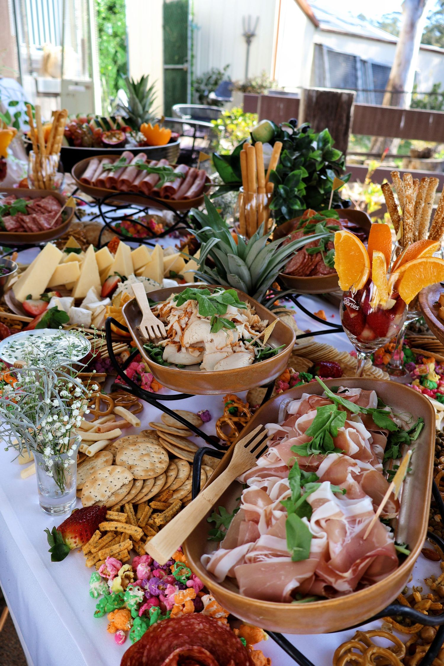 Elaborate outdoor grazing table with charcuterie, cheese, ham, crackers and fresh fruit.