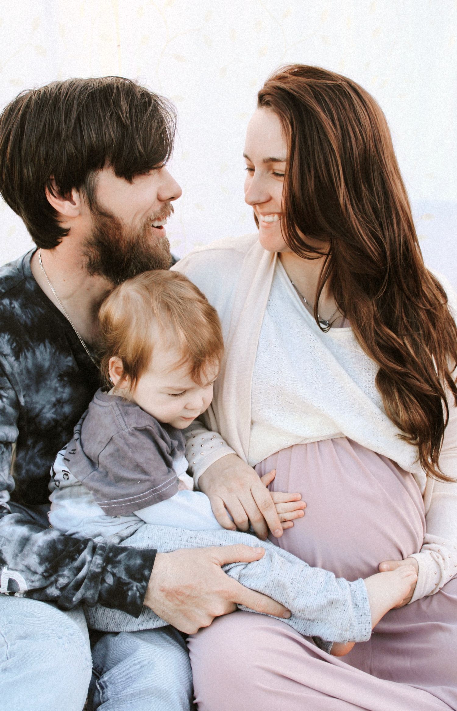 Smiling expectant parents with toddler child share a loving family moment during maternity photo session.