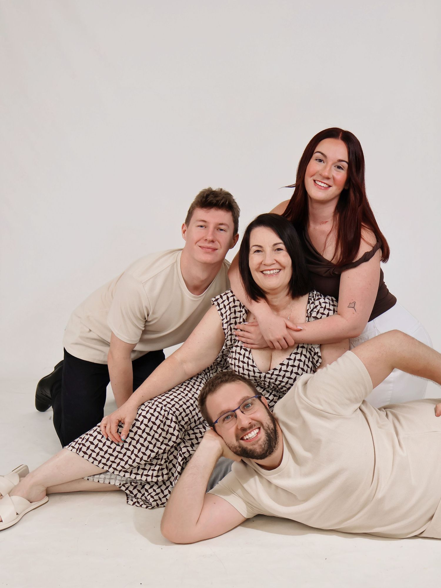 Four family members laughing and stacking playfully on floor in fun white studio photo session.