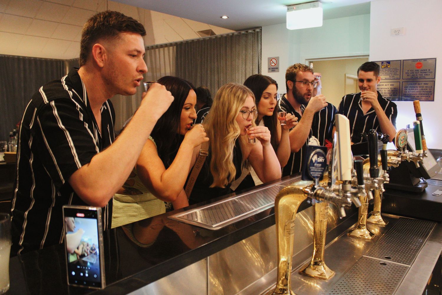 Group of young adults leaning on a bar counter enjoying drinks at a social event.