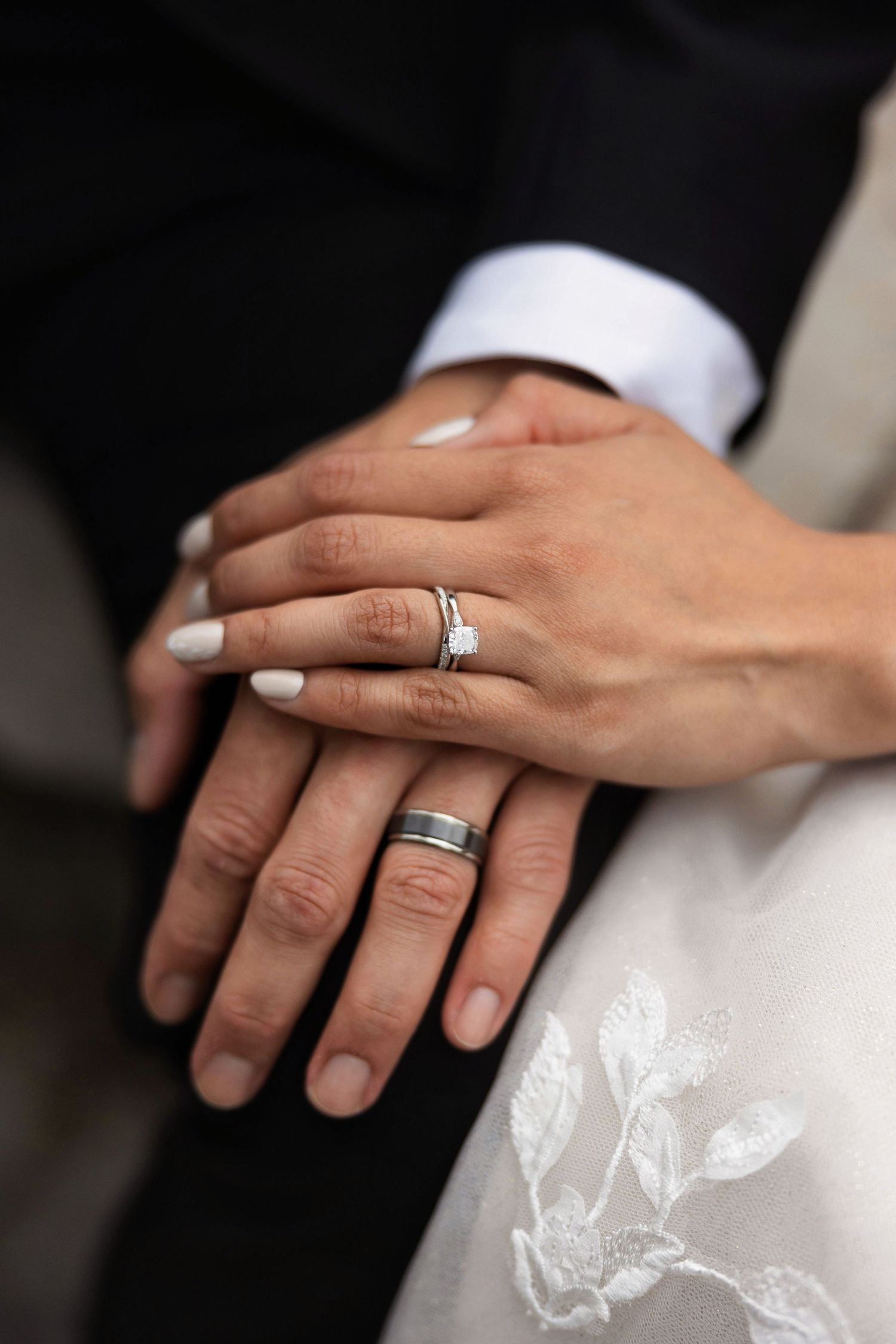 Close-up of newlyweds hands showing wedding rings, bride wearing diamond ring and groom wearing a dark band.