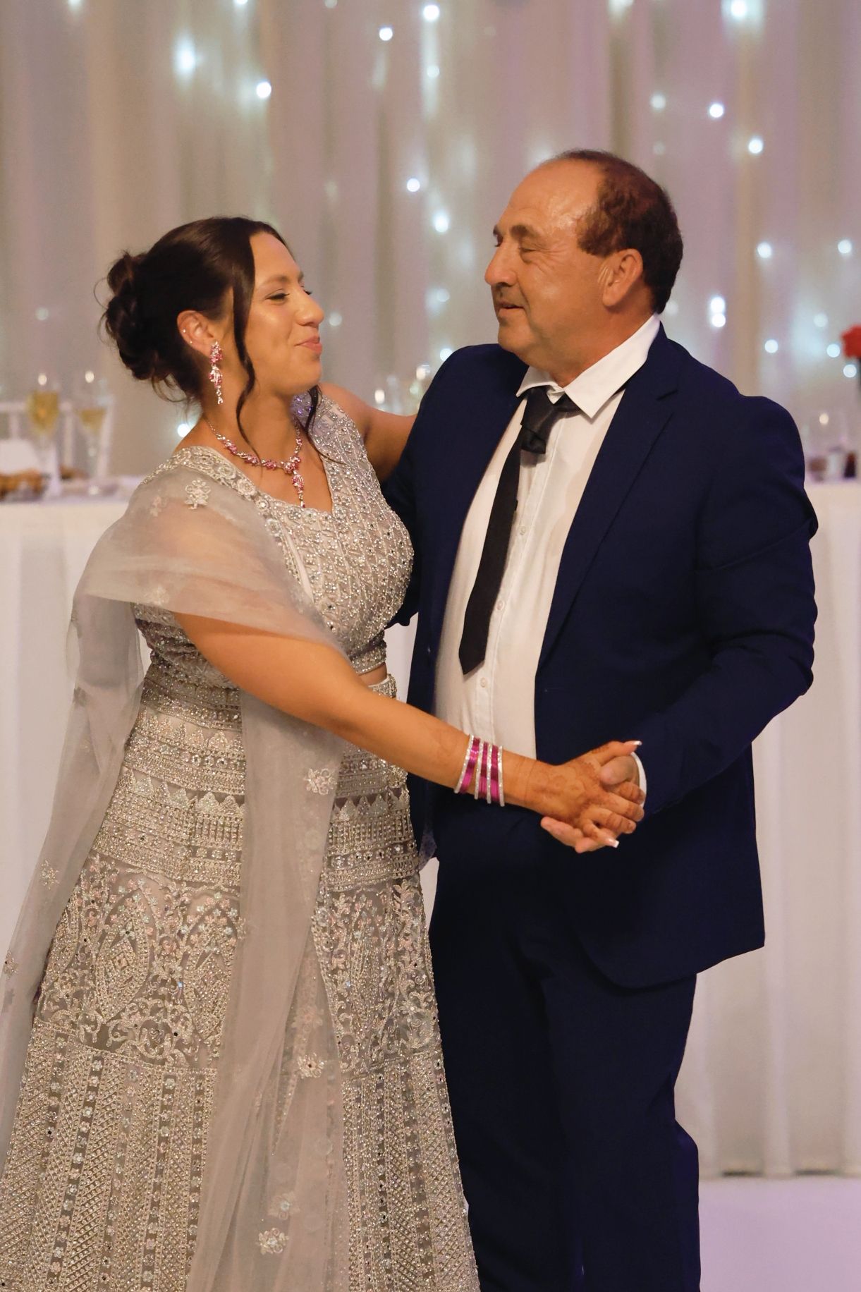 Couple sharing a dance at a formal wedding reception with fairy lights in background.