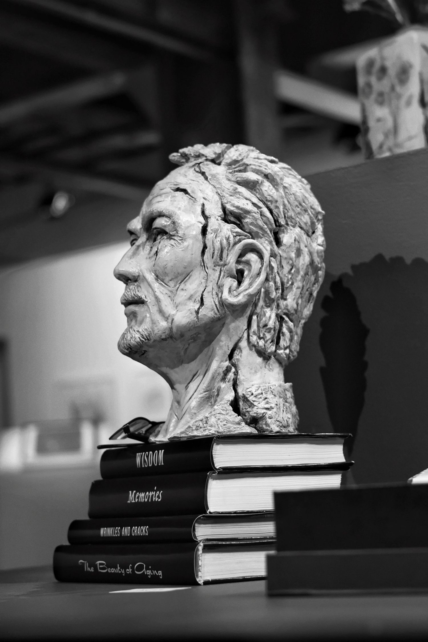 Black and white bust sculpture of an aged man displayed on stacked books in an art exhibition.