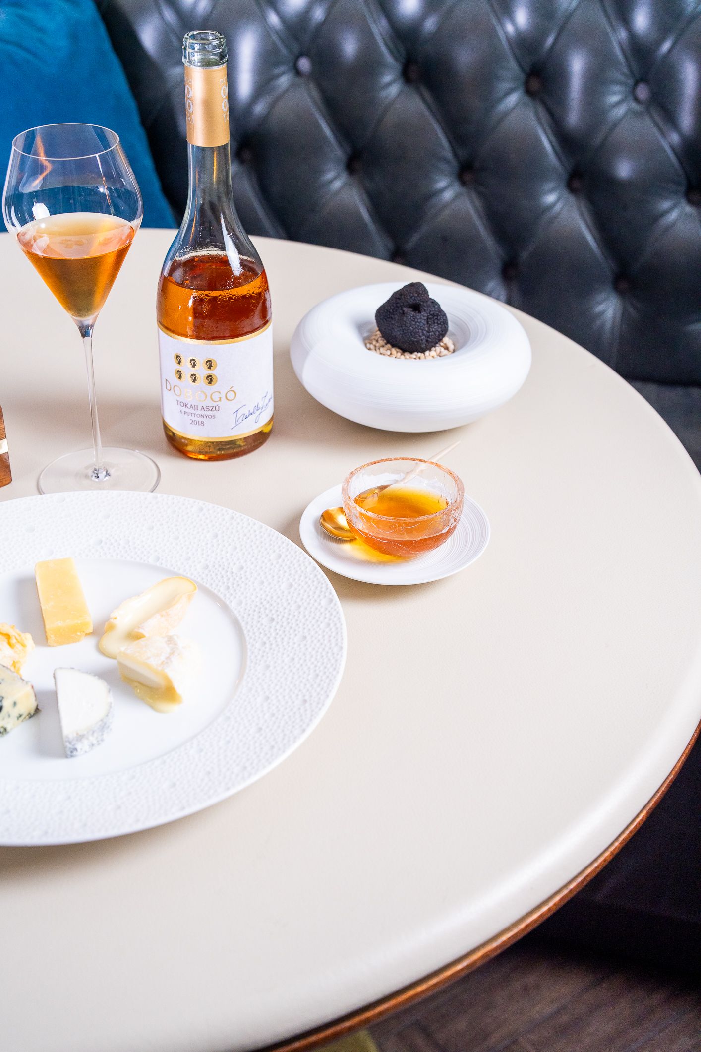 Elegant table setting with rose wine, cheese board, honey, and chocolate dessert on white table.
