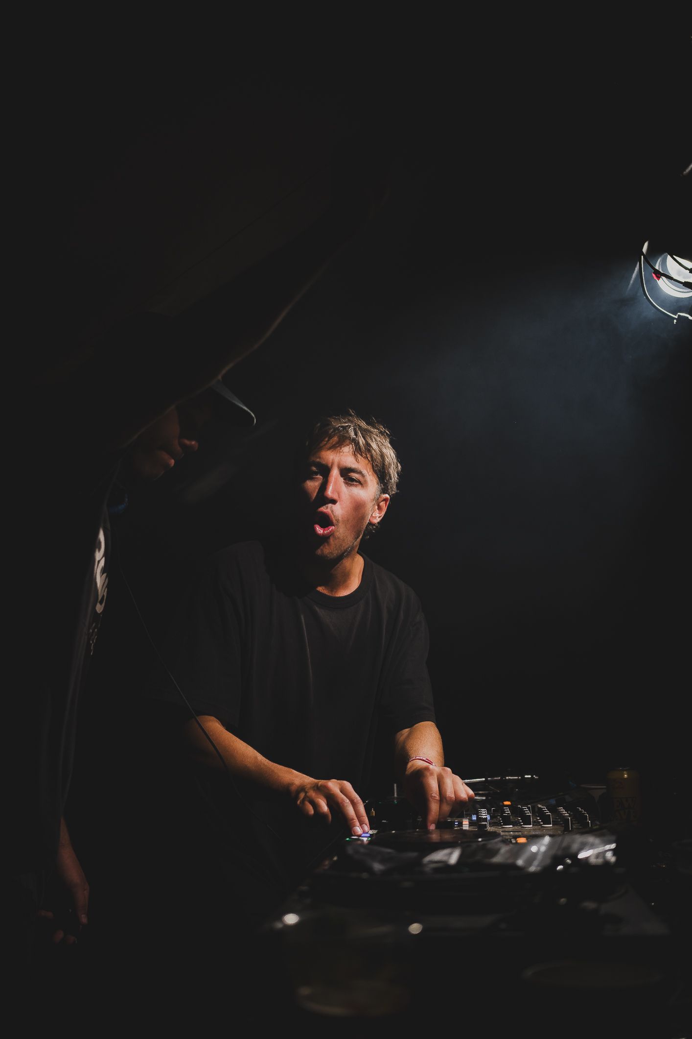 DJ performing energetically at a dark smoky nightclub event.
