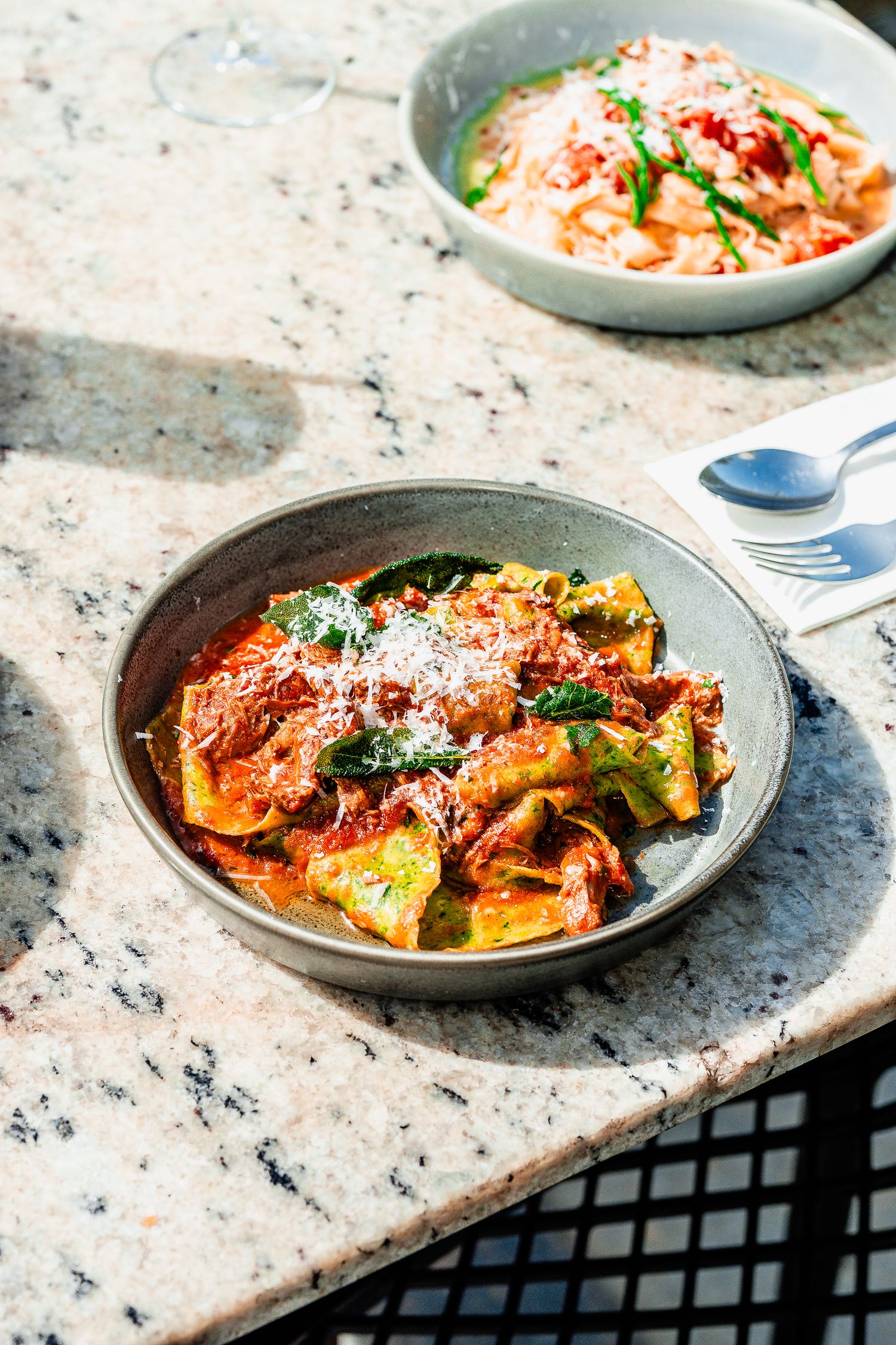 Two bowls of Italian pasta dishes served on a sunlit granite countertop in a restaurant setting.