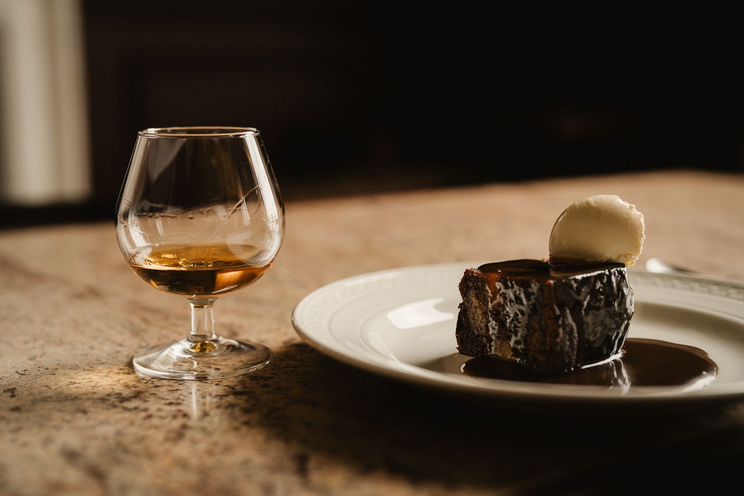 Elegant dessert plate with chocolate cake and vanilla ice cream beside a glass of cognac on a wooden table.