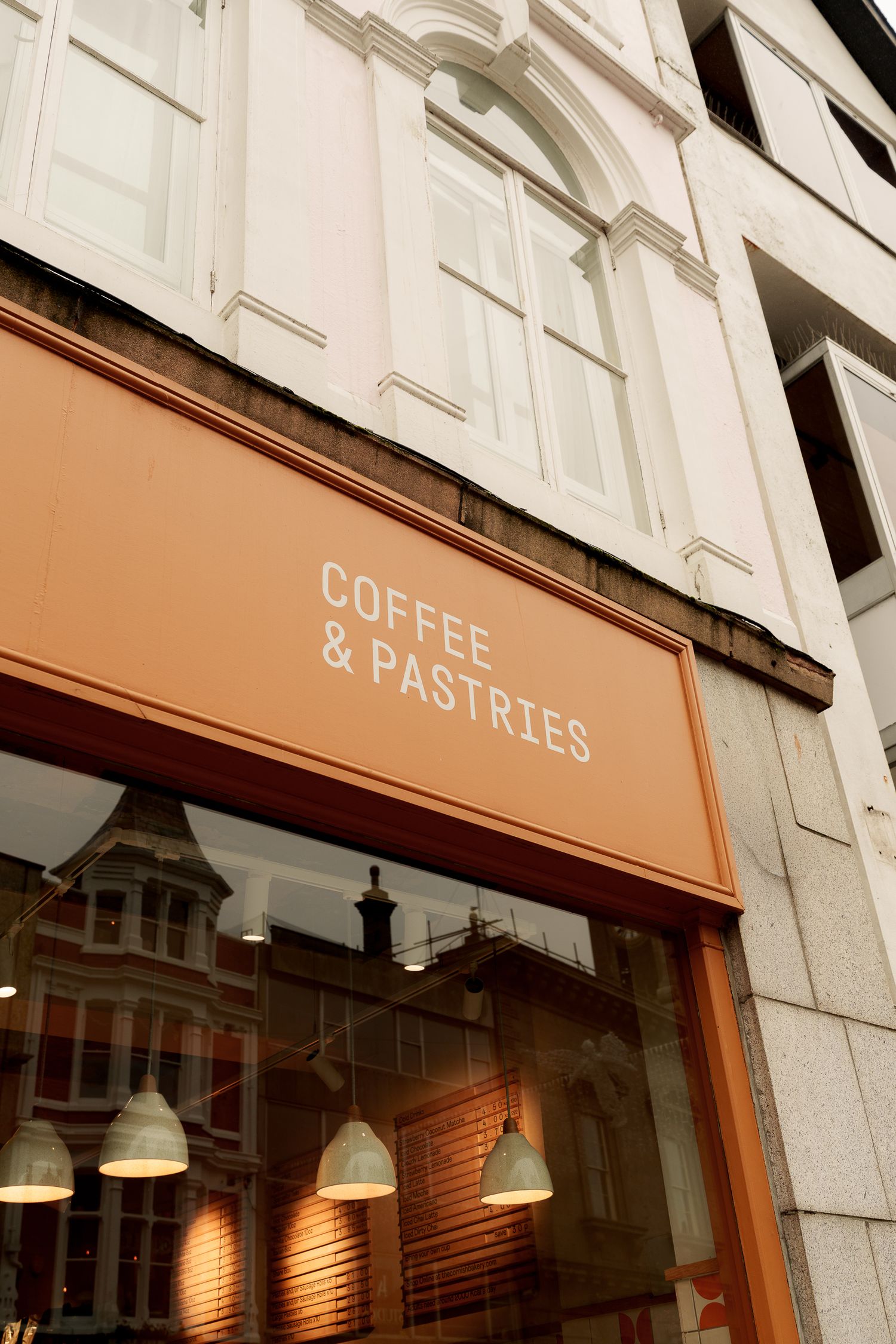 Close-up of an orange Coffee & Pastries cafe storefront sign with pendant lights visible through the window.