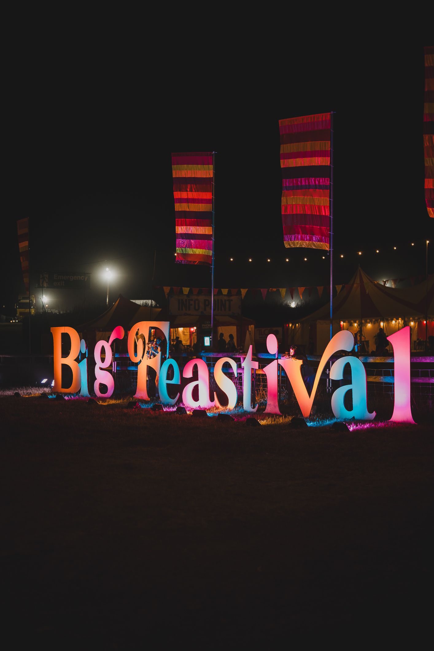 Illuminated Big Feastival sign with colorful letters and striped flags at a night food festival.