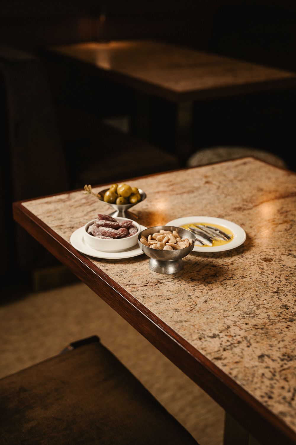 Spanish tapas spread with olives, anchovies, and nuts on a marble bar counter.