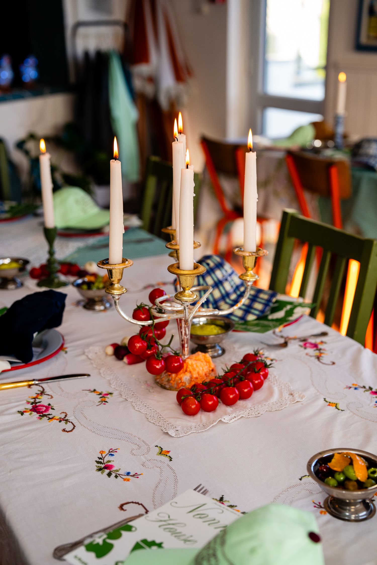Elegant dining table set with candelabra, cherry tomatoes, and embroidered linen tablecloth with lit candles.