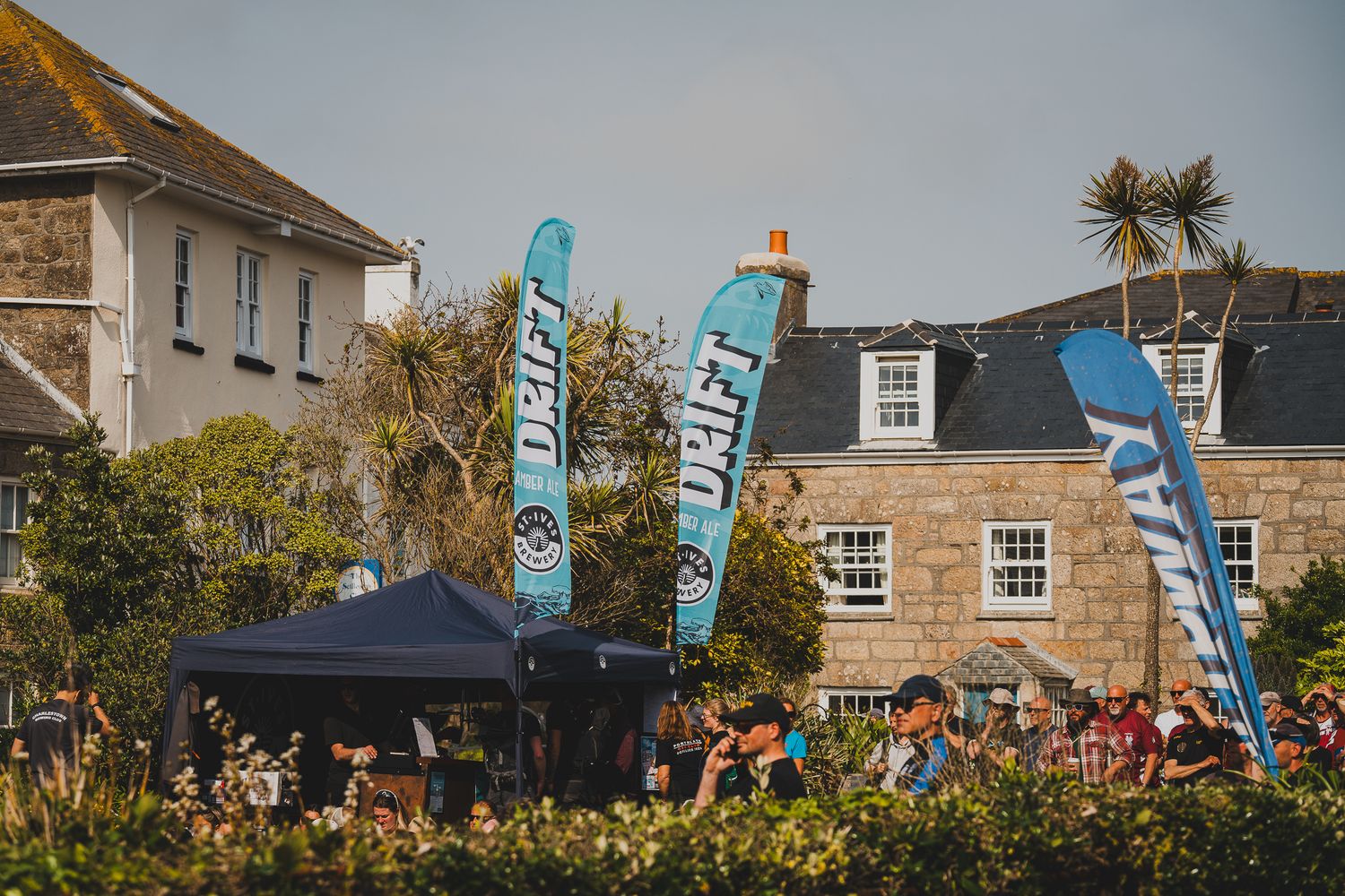 Colorful Drift branded banners flying above a crowd at an outdoor festival near stone buildings.