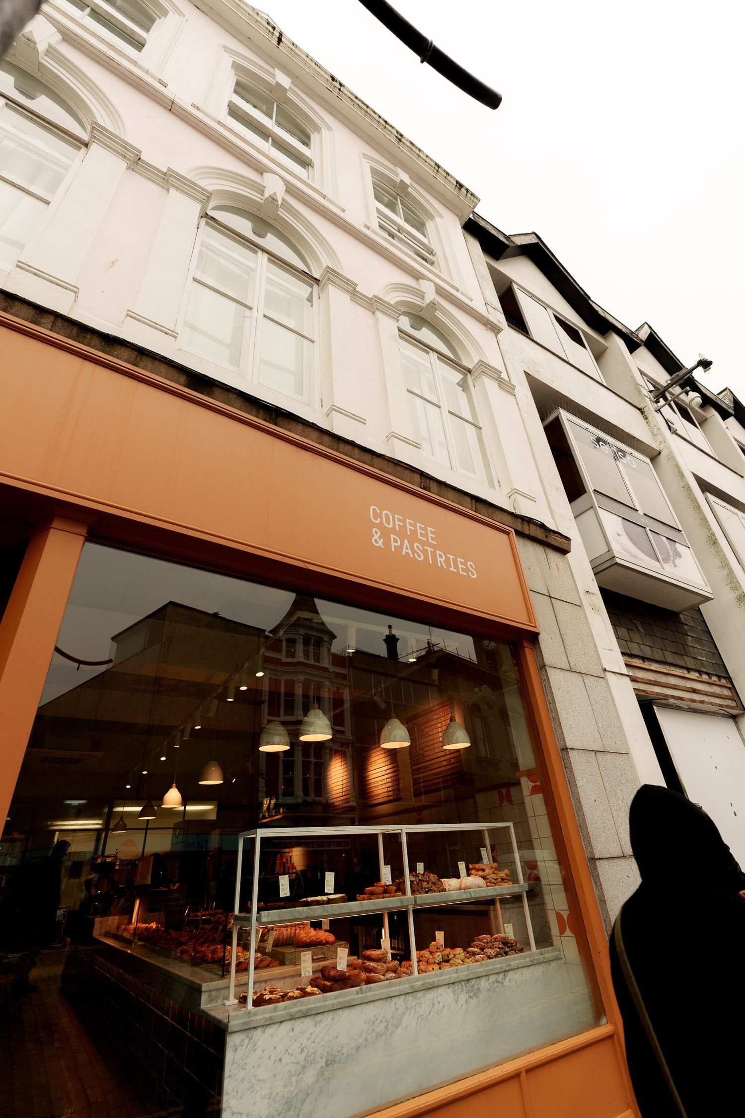 Low-angle view of Coffee & Pastries cafe exterior with pastries displayed in the window.
