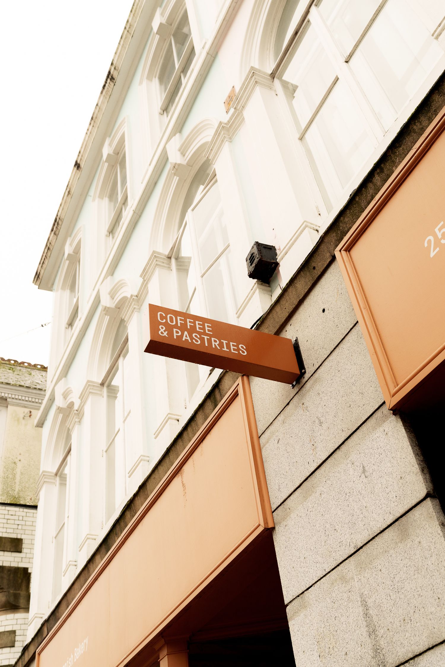 Side angle view of Coffee & Pastries cafe orange signage mounted on a stone building exterior.