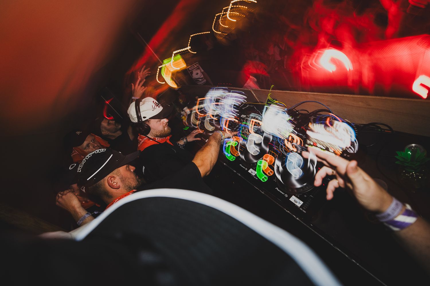 DJ performs under red lights for an energetic crowd at a nightclub event.