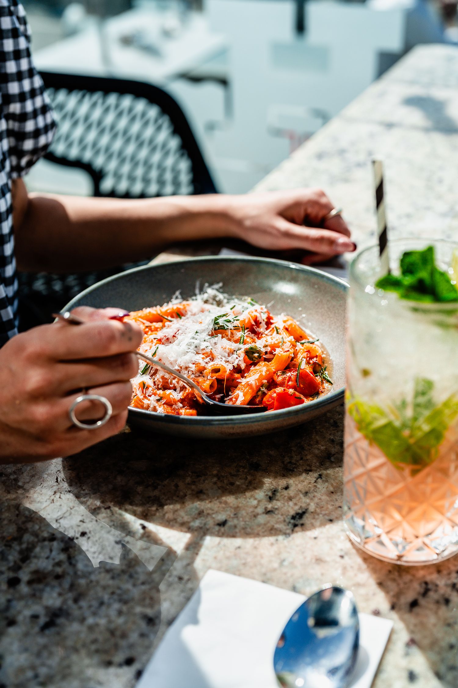 Woman dining on a bowl of penne pasta with tomato sauce and parmesan at a marble restaurant counter.