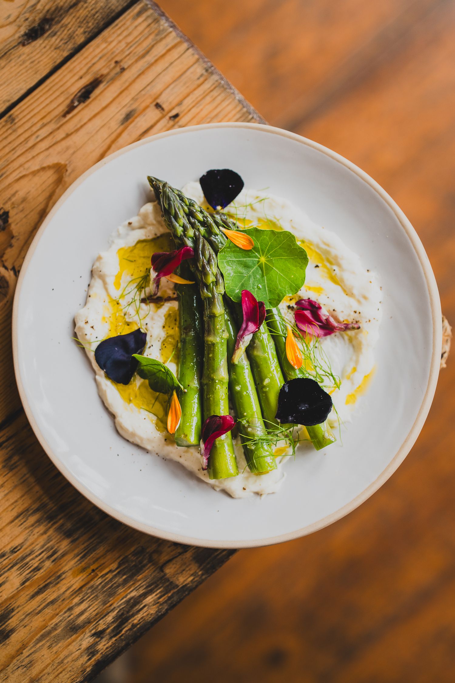 Elegant asparagus dish with edible flowers on white plate atop wooden table.