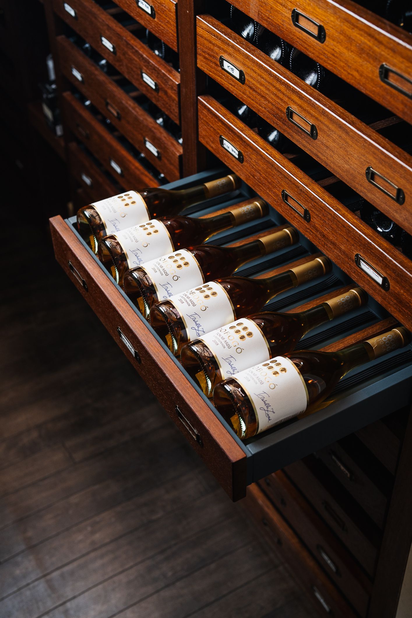 Wine bottles stored horizontally in open wooden drawer of a classic cellar storage cabinet.