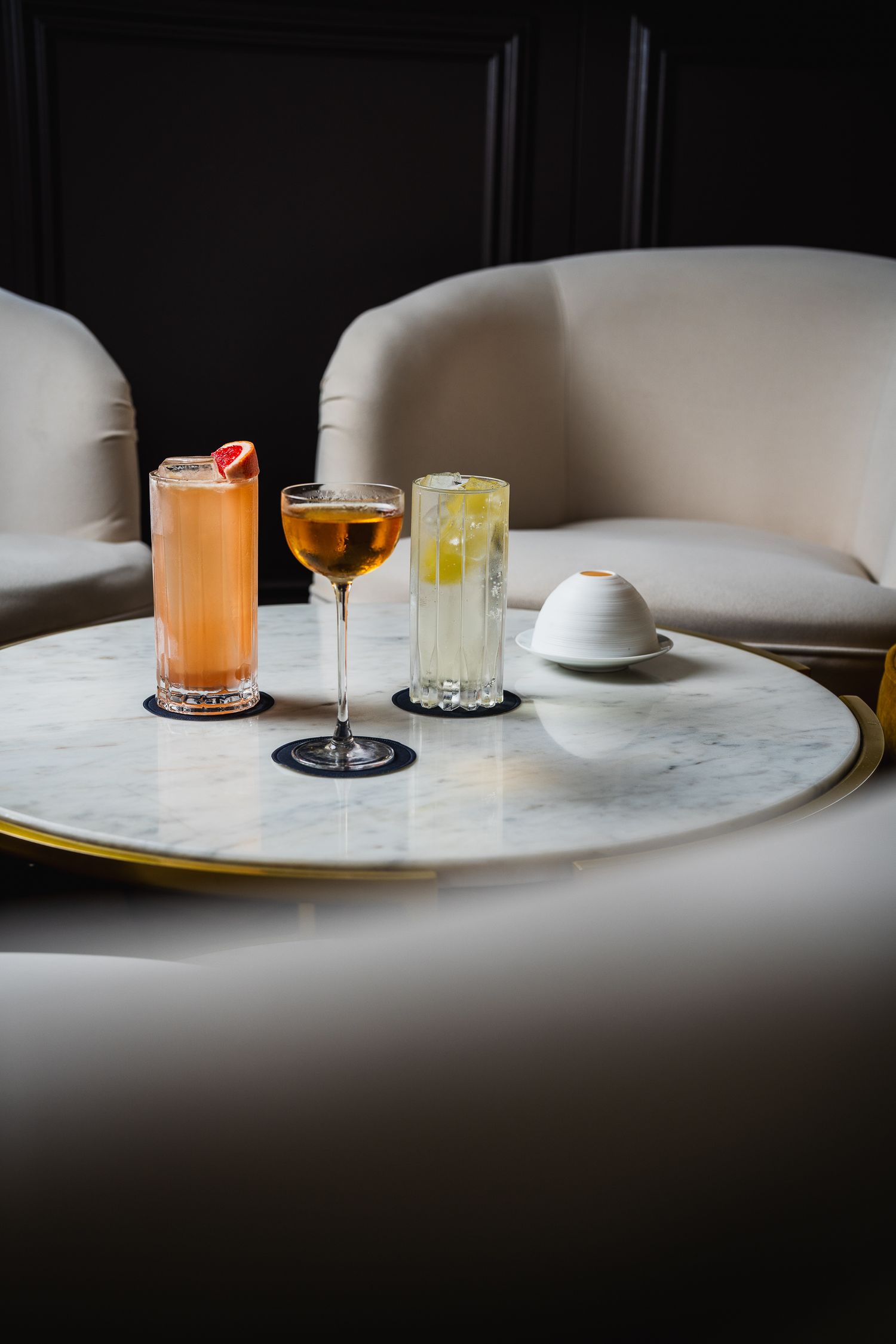 Three elegant cocktails on a marble table in a sophisticated upscale bar lounge setting.
