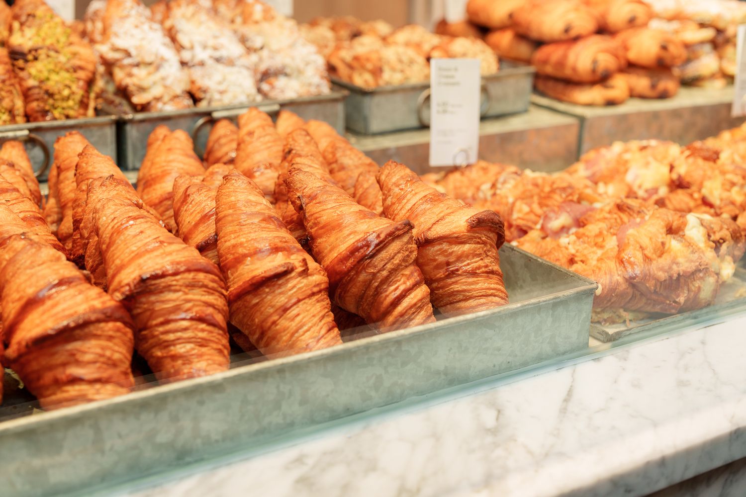 Fresh golden croissants and pastries displayed in a bakery glass counter case.