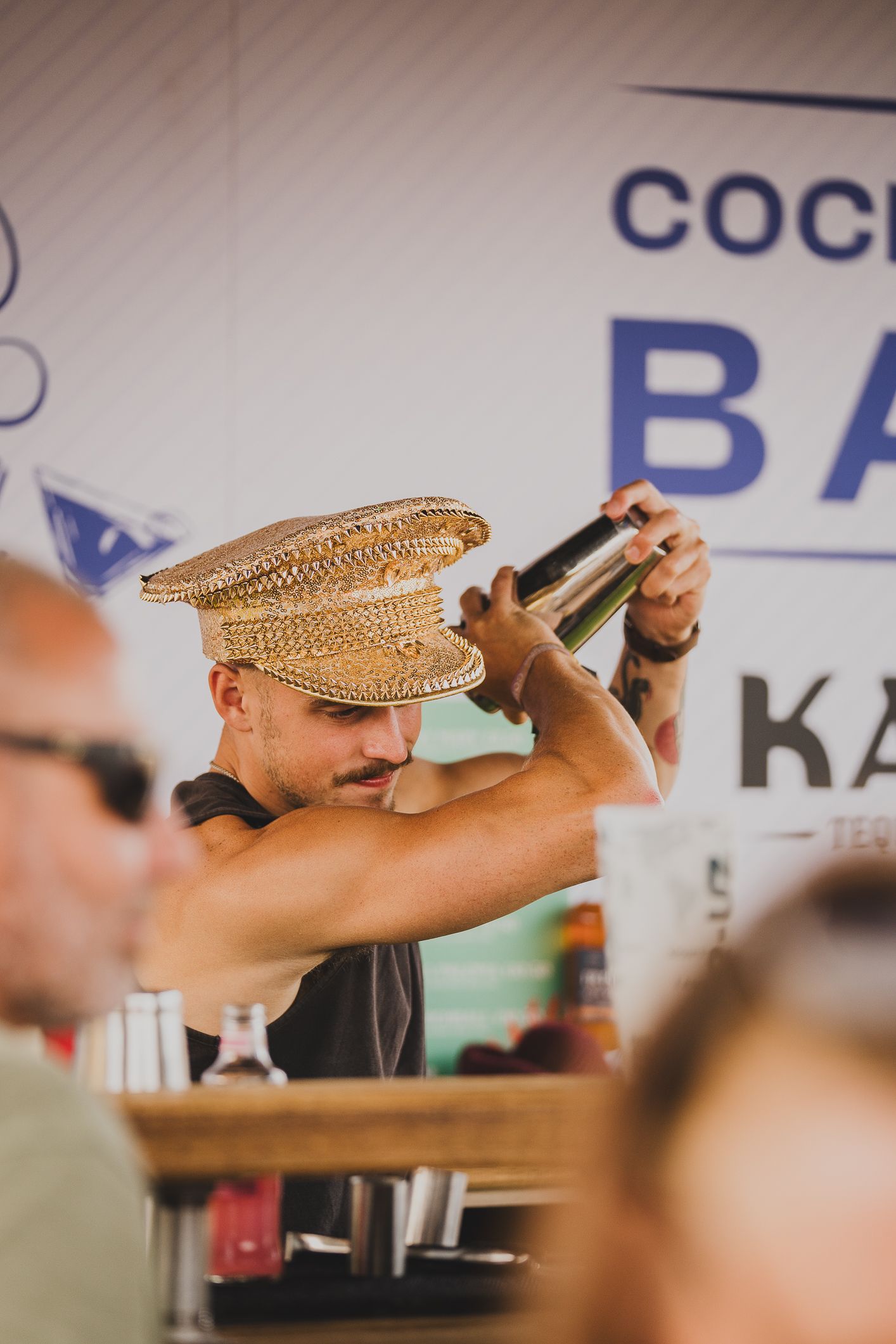 Bartender in gold sequin hat mixing cocktails at a festival cocktail bar competition.