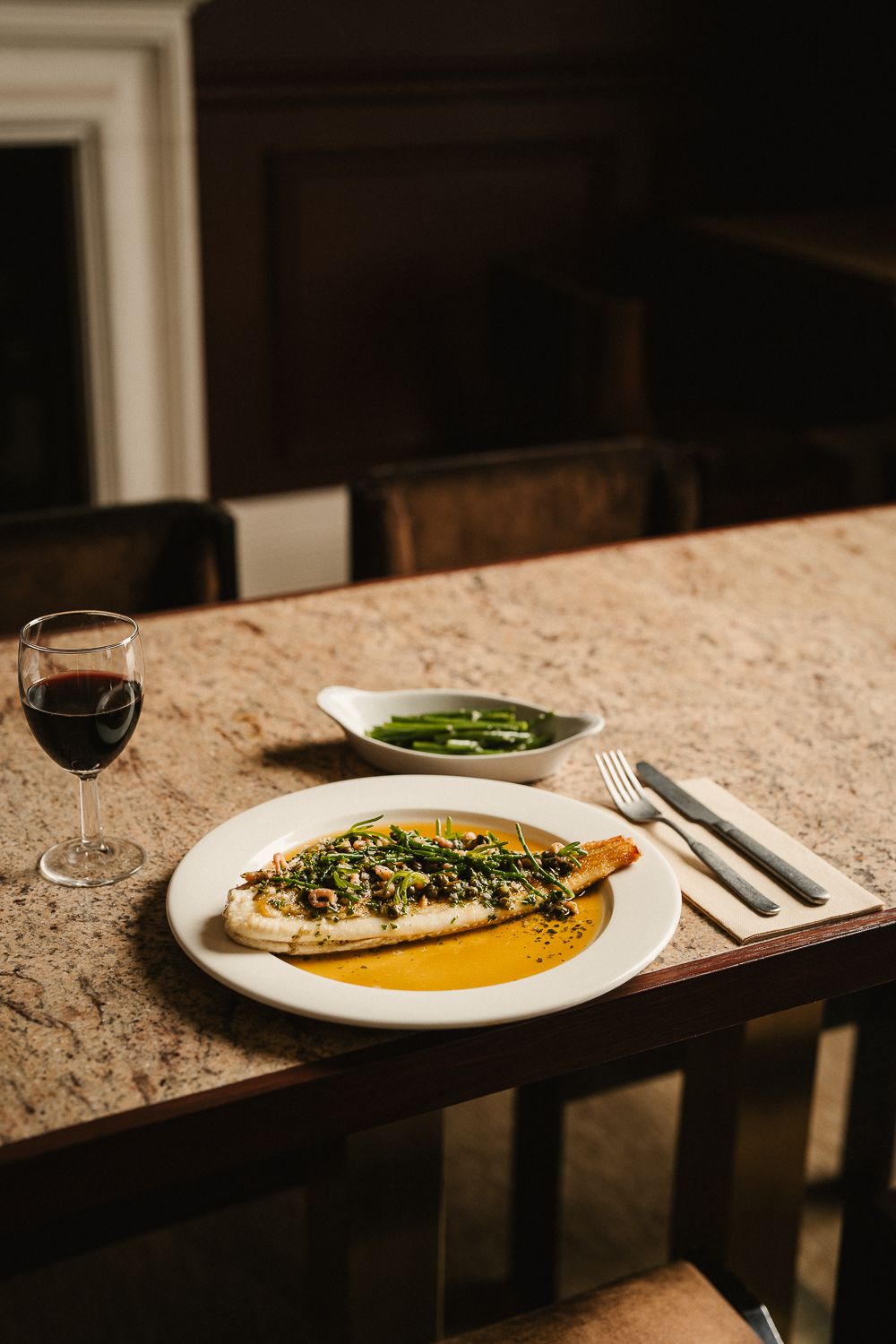Whole roasted fish in saffron sauce with capers served alongside green beans and red wine.