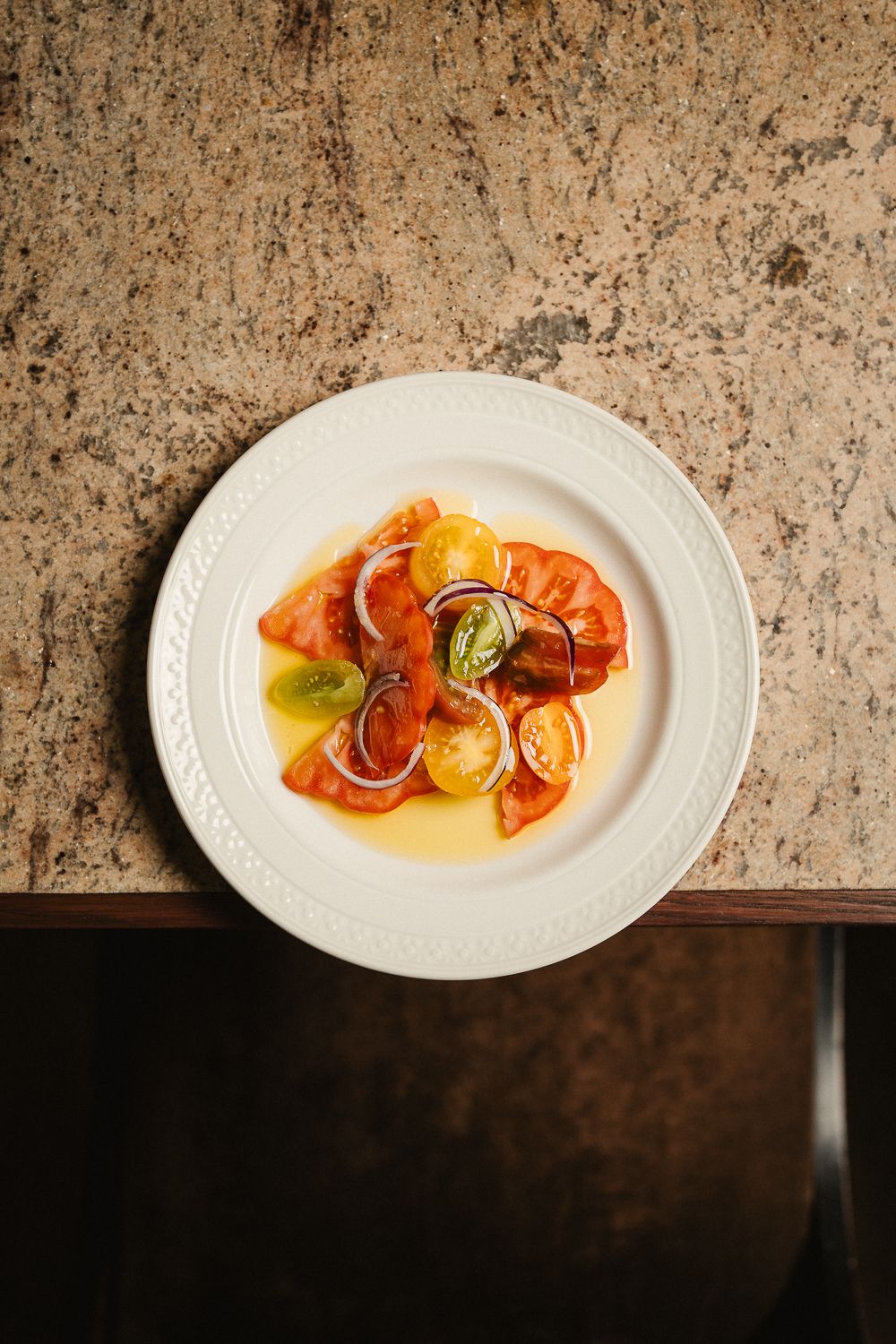 Vibrant heirloom tomato salad with red onion and fresh herbs on white plate.