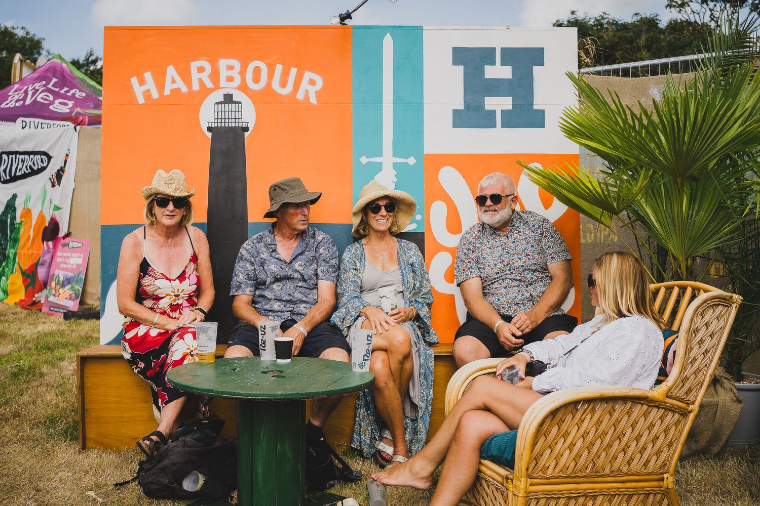 Four adults sit and chat in front of a colorful Harbour branded mural at an outdoor festival.