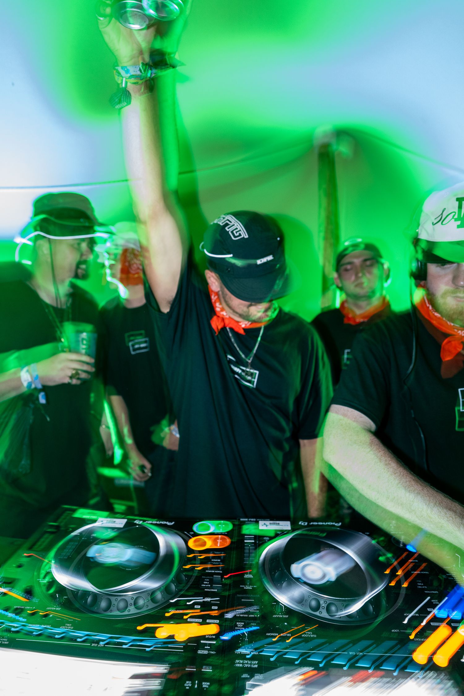 DJ raises a trophy under green lights while crowd cheers at an energetic event.