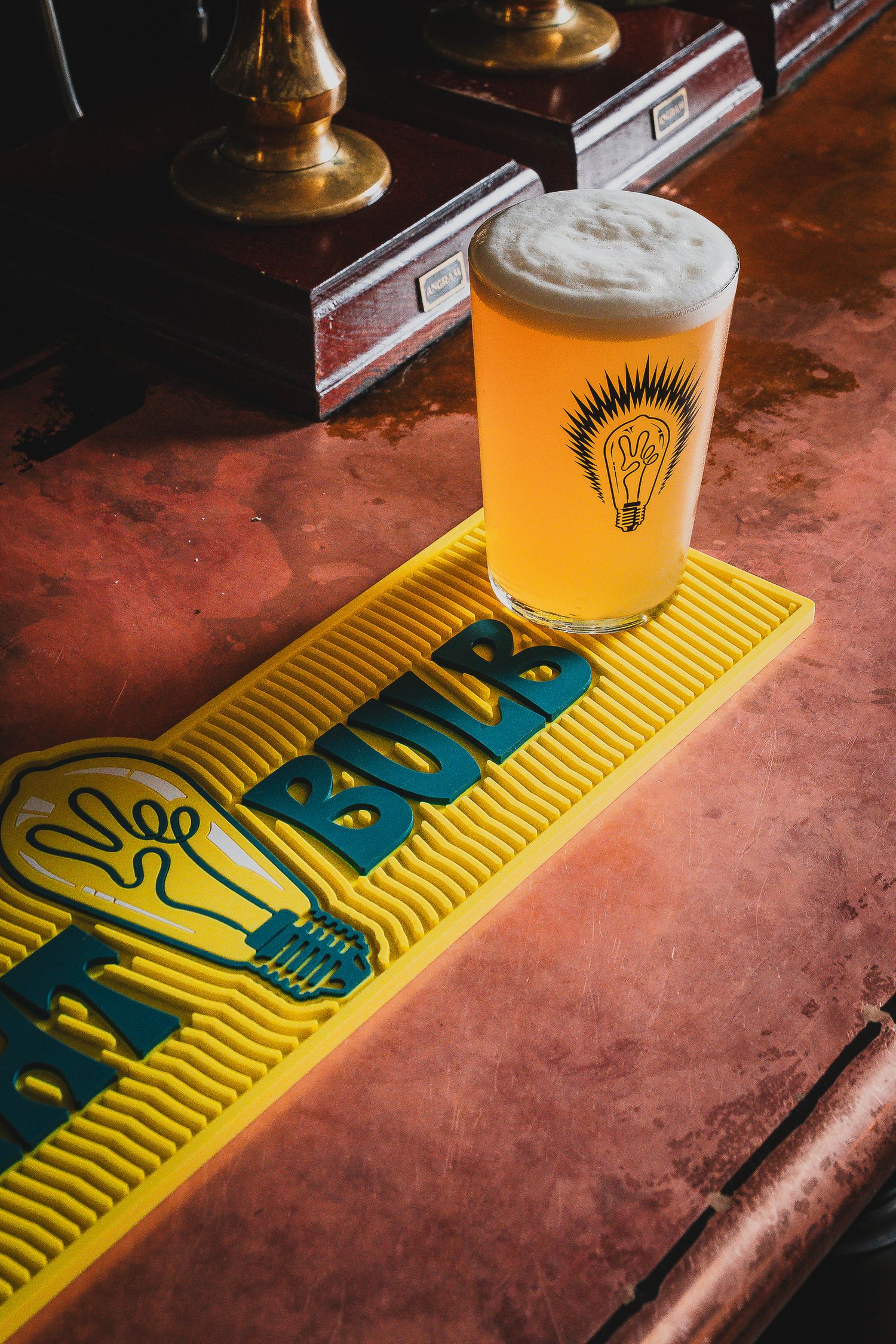 Hazy pale ale in Bulb branded pint glass on yellow bar mat on copper bar counter.