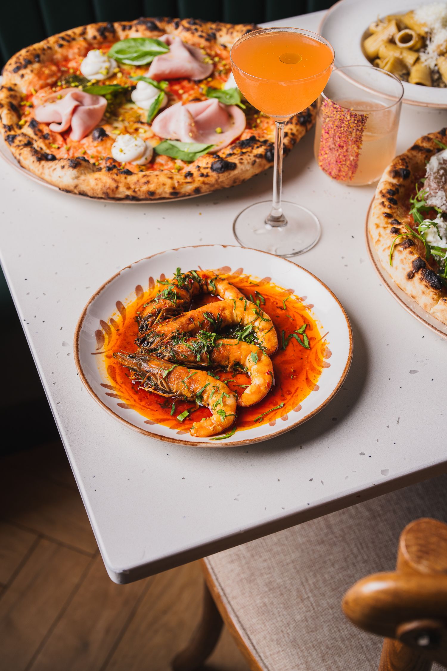 Restaurant table with shrimp in tomato sauce, Neapolitan pizzas, pasta, and an Aperol spritz.