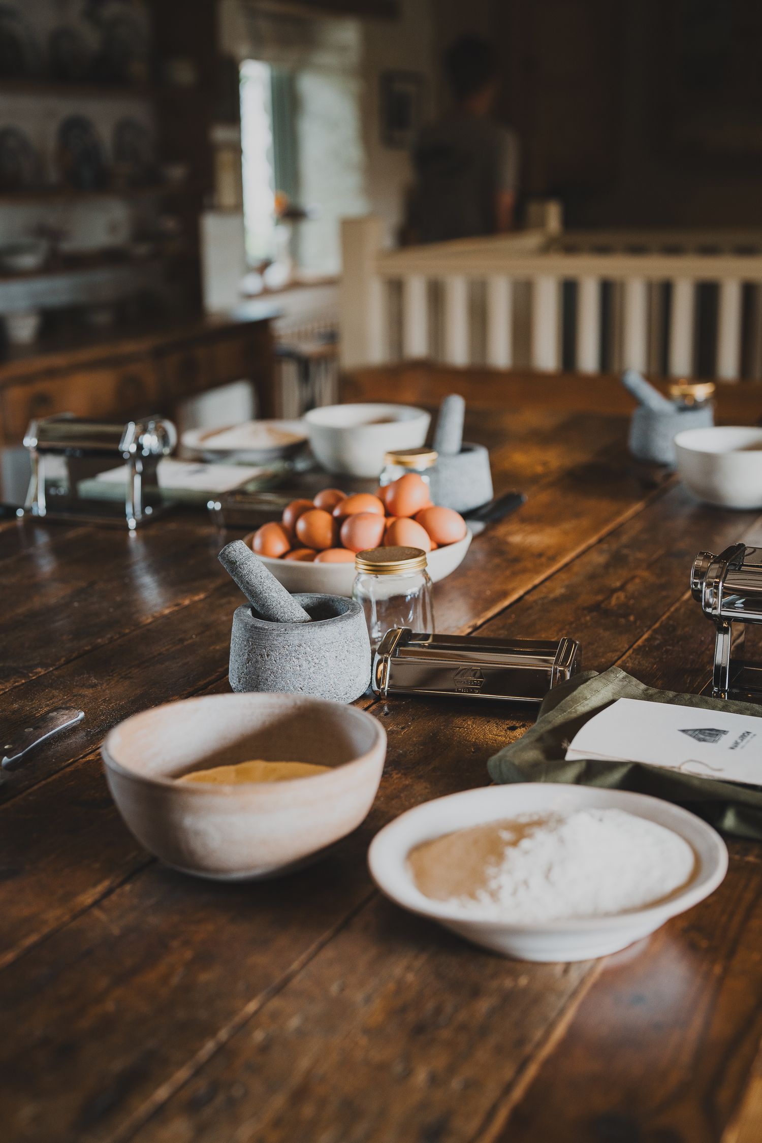 Rustic wooden table set with eggs, flour, bowls, and pasta-making tools for a cooking class.