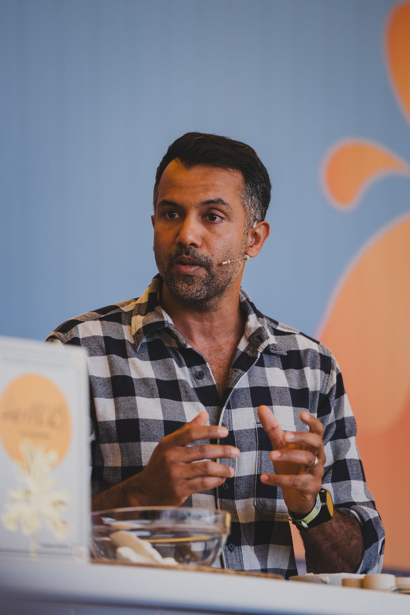 Man in plaid shirt speaking with a microphone at a food or business event.