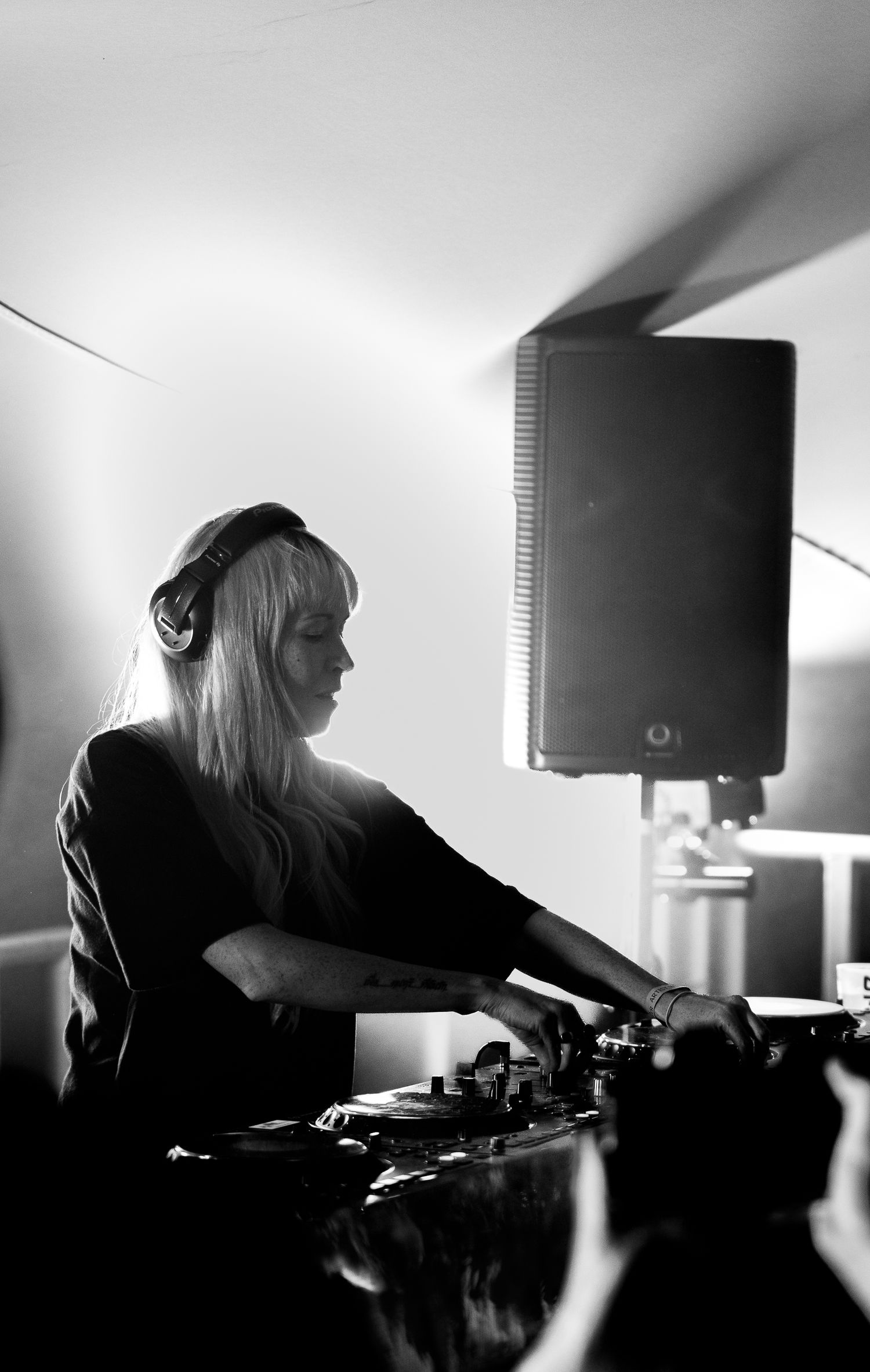 Black and white photo of a female DJ mixing tracks with headphones at decks.