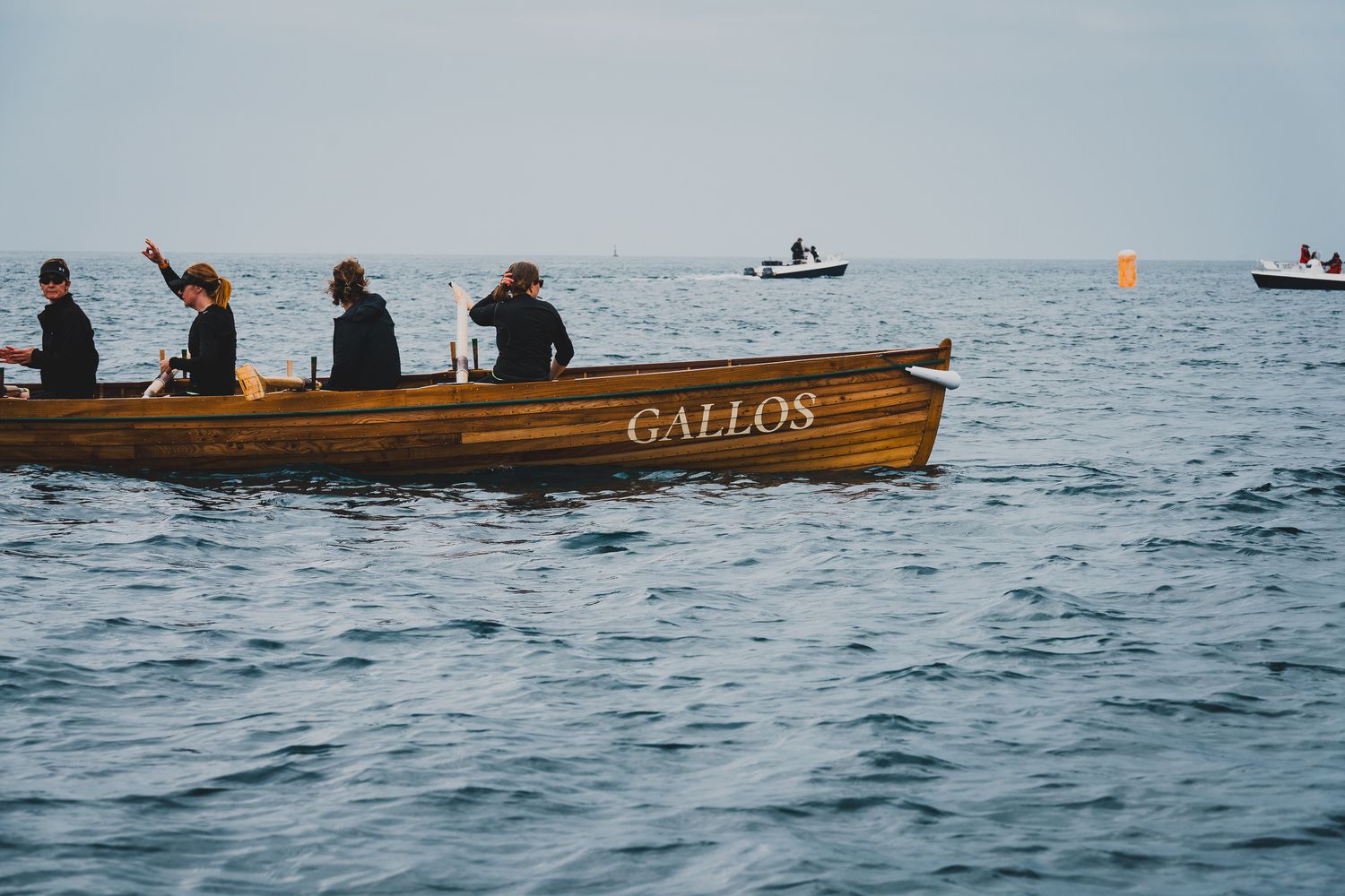 Crew members rowing the wooden Gallos pilot gig boat across open ocean waters during a race.