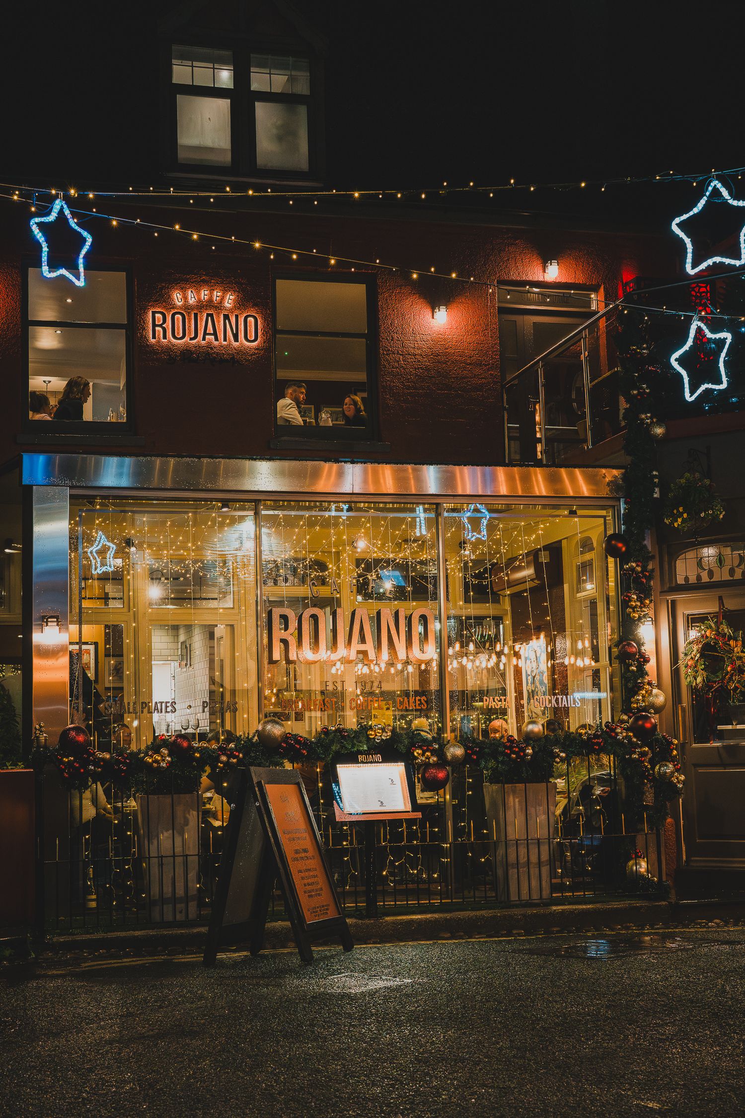 Rojano's restaurant exterior at night with festive fairy lights and neon star decorations in Manchester.