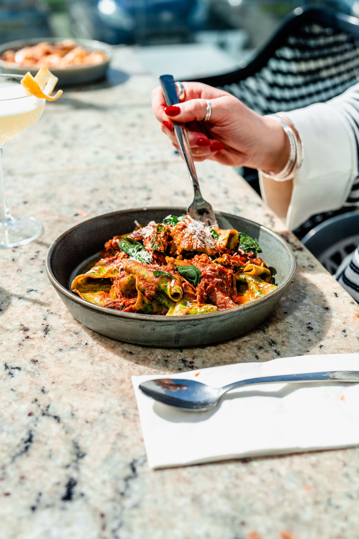 Woman eating rigatoni pasta in tomato meat sauce with fresh basil and parmesan cheese.