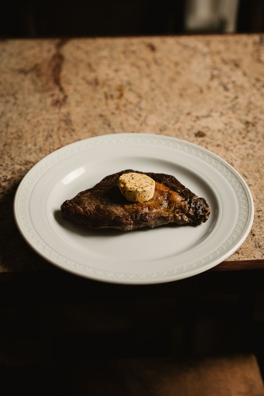 Perfectly seared steak topped with herb compound butter on white ceramic plate.