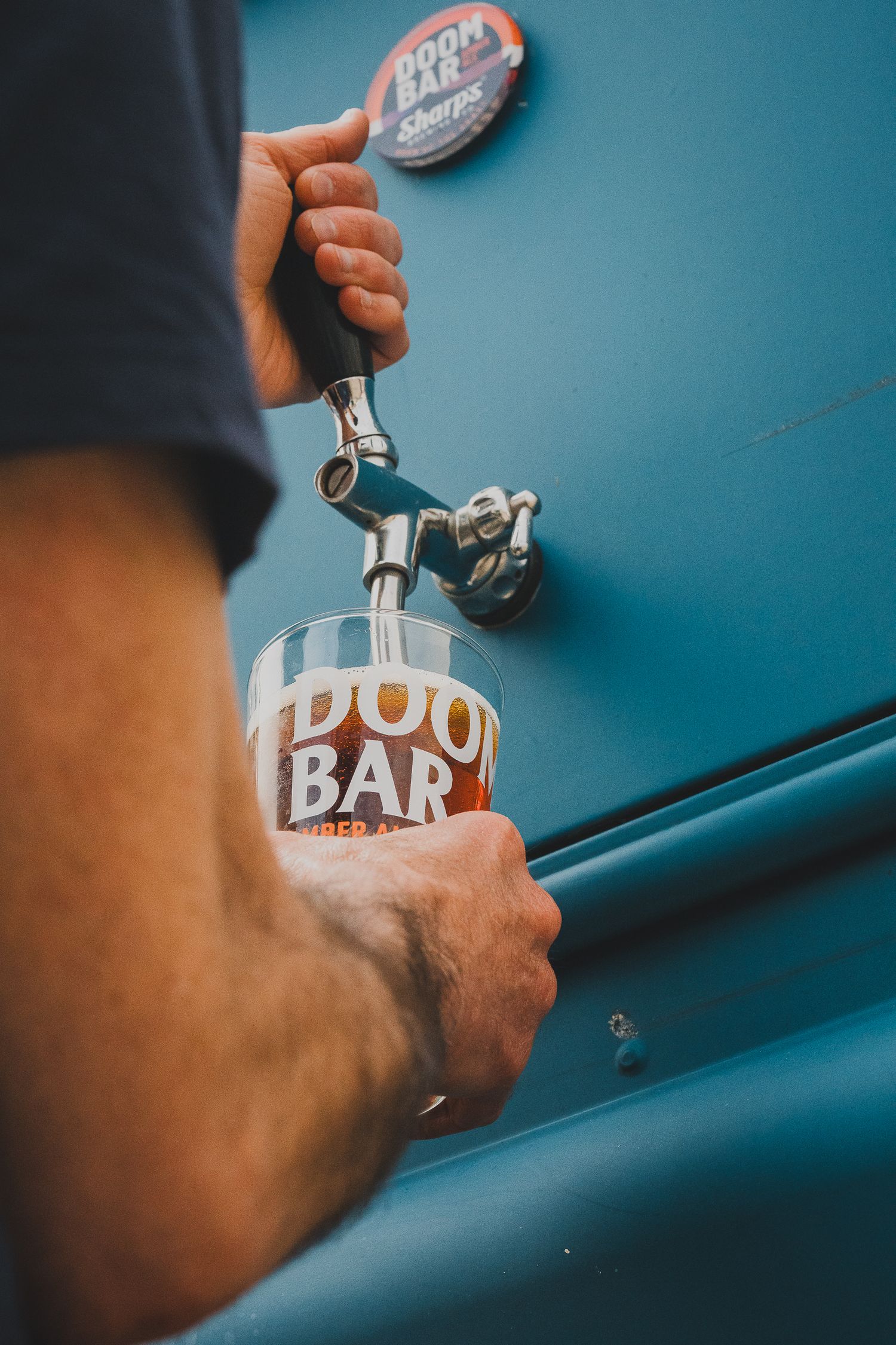 Bartender pouring Doom Bar ale from tap into branded pint glass.