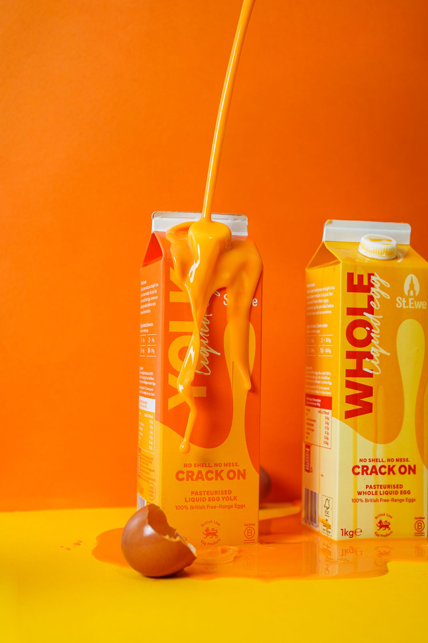 Two orange cartons of whole liquid egg product with egg yolk splash on vibrant orange background.